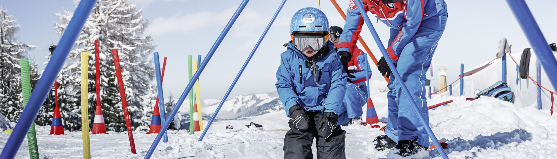 Ein Dutzend Skischulen in Flachau, Wagrain und St. Johann-Alpendorf mit mehrsprachigen Skilehrern bieten beste Übungsvoraussetzungen für Kinder ebenso wie für Erwachsene. | © Armin Walcher, Skischule Alpendorf Kleiner Skifahrer fährt gemeinsam mit einem Skilehrer durch Übungsstangen im Kinderland Alpendorf im Skigebiet Snow Space Salzburg. | © Armin Walcher, Skischule Alpendorf