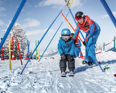 Kleiner Skifahrer fährt gemeinsam mit einem Skilehrer durch Übungsstangen im Kinderland Alpendorf im Skigebiet Snow Space Salzburg. | © Armin Walcher, Skischule Alpendorf