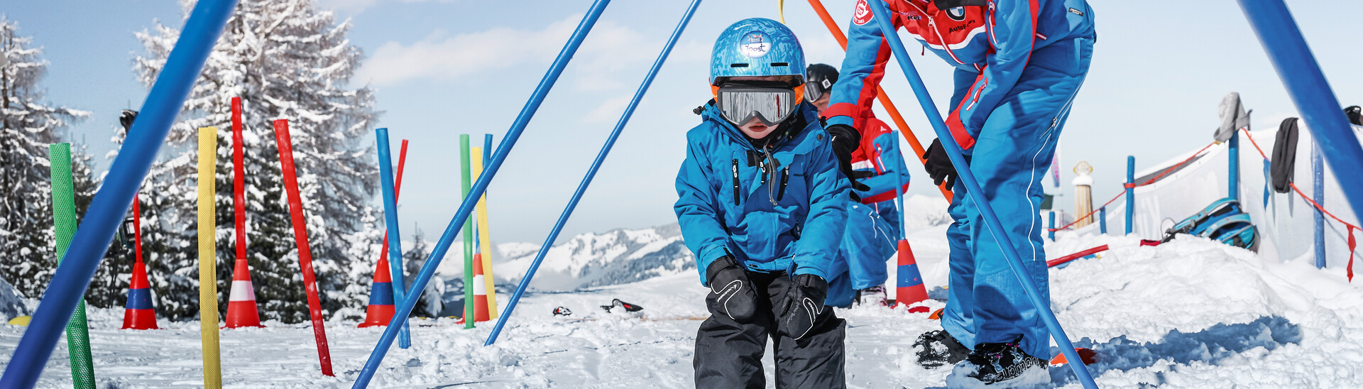 Small kid skiing through practice gates together with a skiing instructor at Alpendorf Kinderland at Snow Space Salzburg ski resort | © Armin Walcher, Skischule Alpendorf