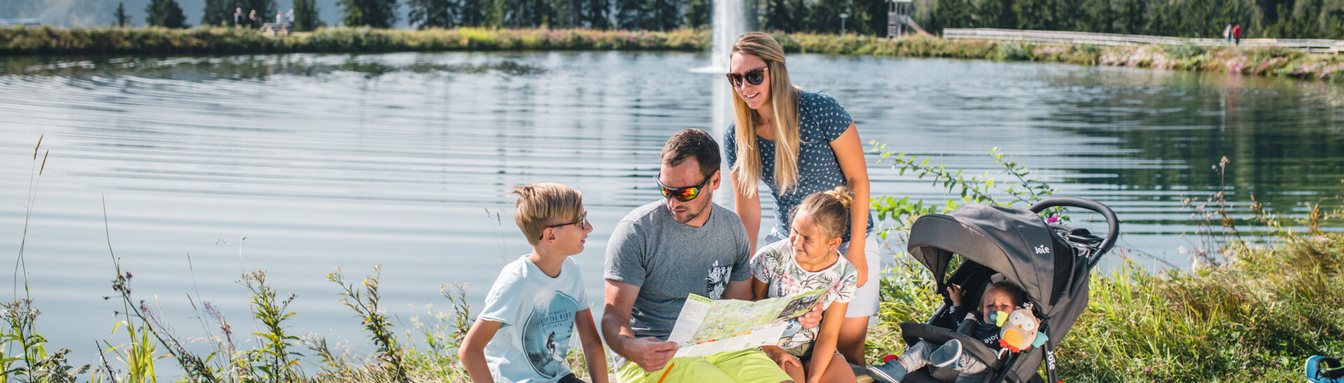 Family in front of a mountain lake orientating with a map in Snow Space Salzburg 