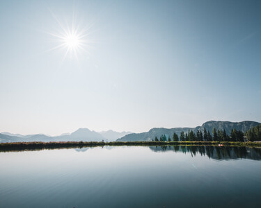 Soothing view of a crystal-clear mountain lake at Snow Space Salzburg under a bright blue sky with the sun at its zenith