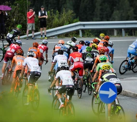 Cyclists in colourful jerseys take part in a race on a winding road at Snow Space Salzburg